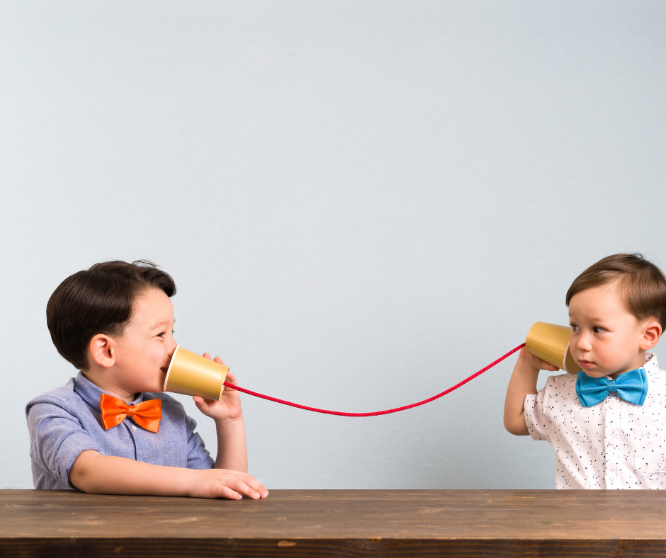 Two little boys with bowties using cups and string as a telephone